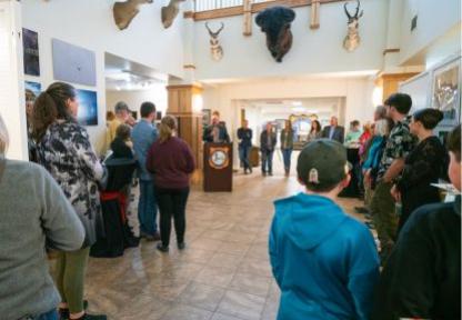 A crowd turns their attention to the Game and Fish Director delivering remarks from a podium at an event at the Wyoming Game and Fish Department's headquarters.