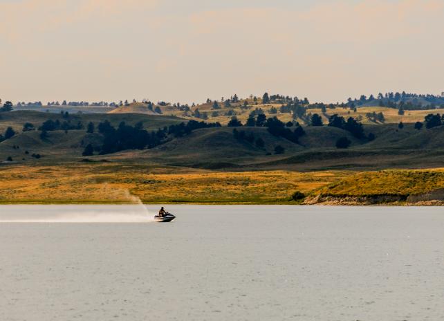 A person on a jet ski moves quickly over the water at Grayrocks reservoir. Rolling hills are visible in the background.