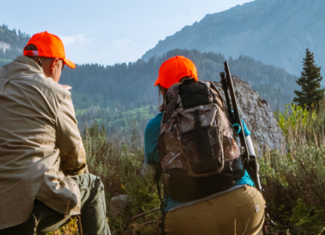 Two hunters in hunter orange hats sneak up on their quarry in a beautiful mountainous landscape.