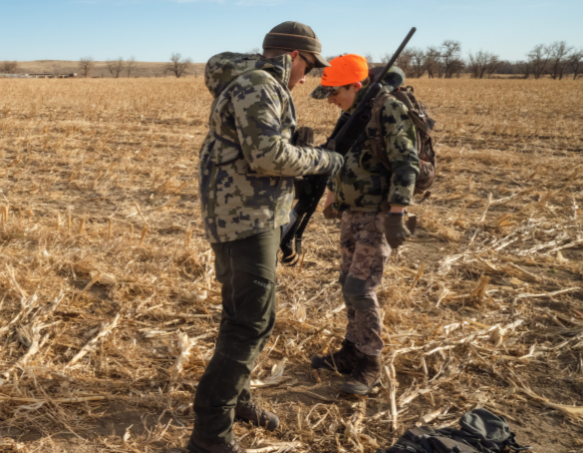 A mento assists a youth hunter in a field as they prepare for a deer hunt.