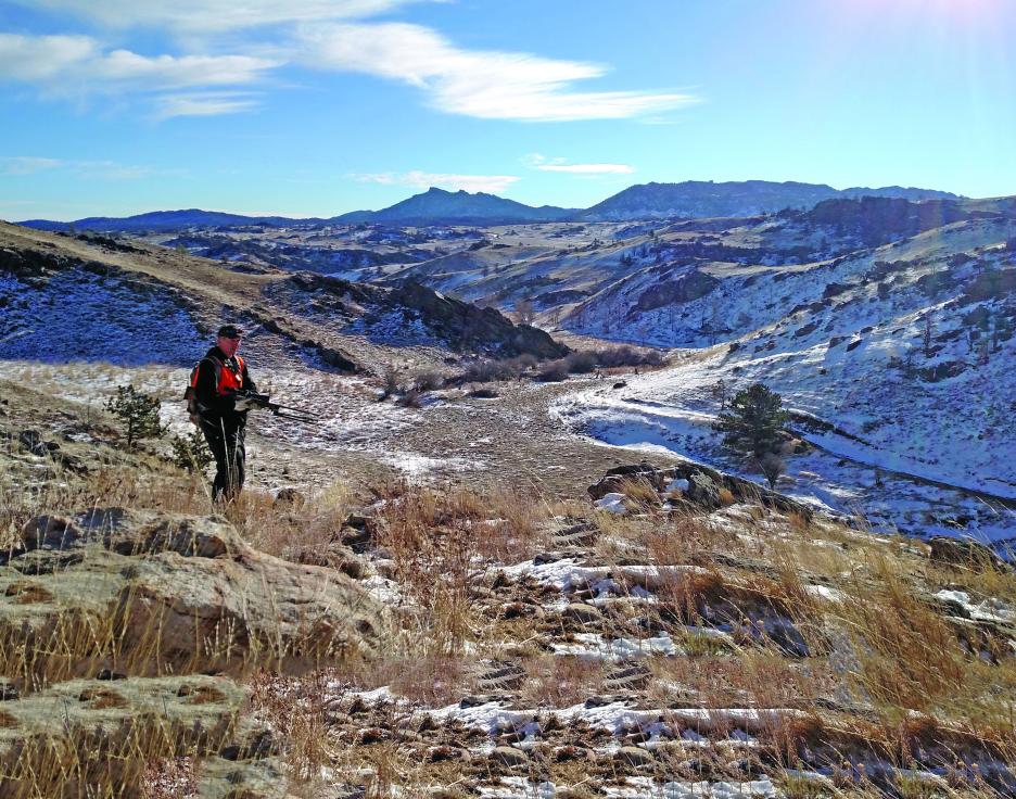 A hunter walks across mountainous public access terrain.