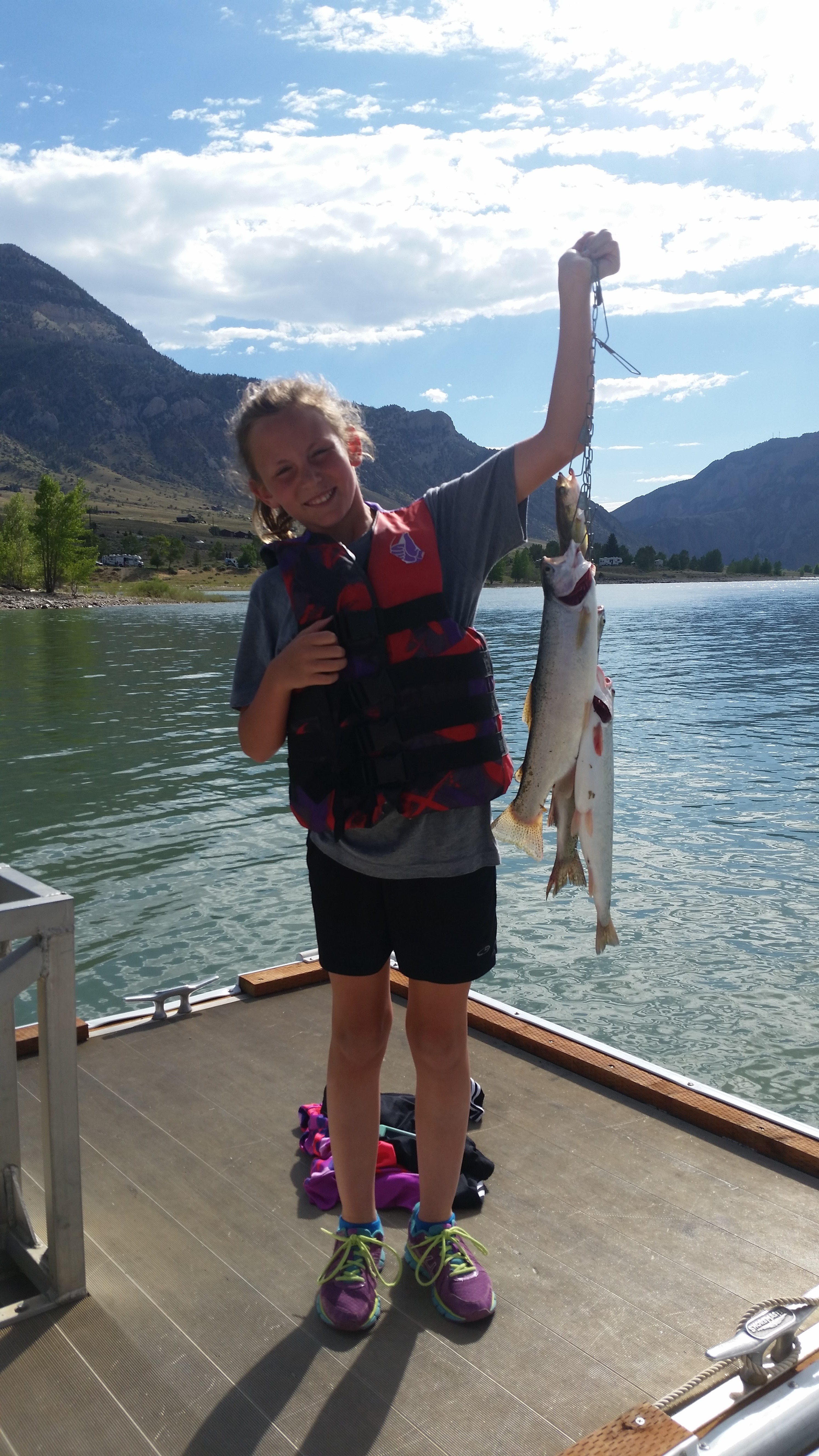 Girl with a life jacket holding up three large trout on stringer