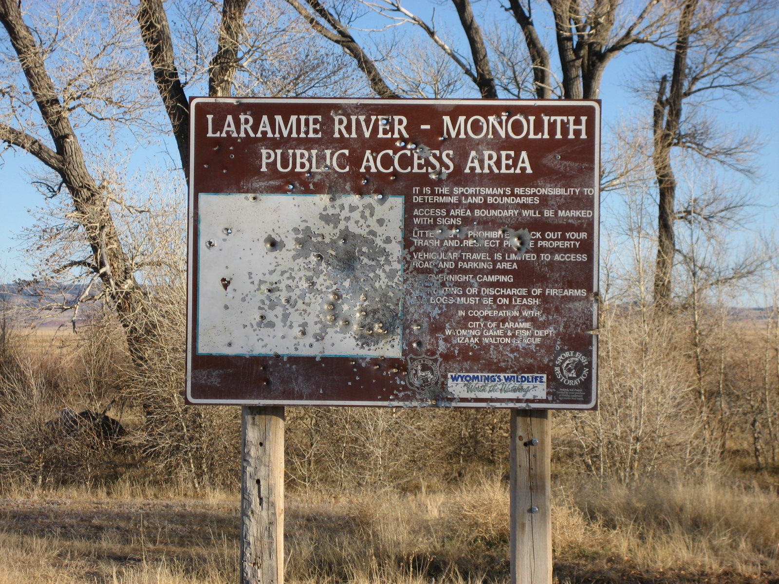 a metal sign that is illegible from bullet holes