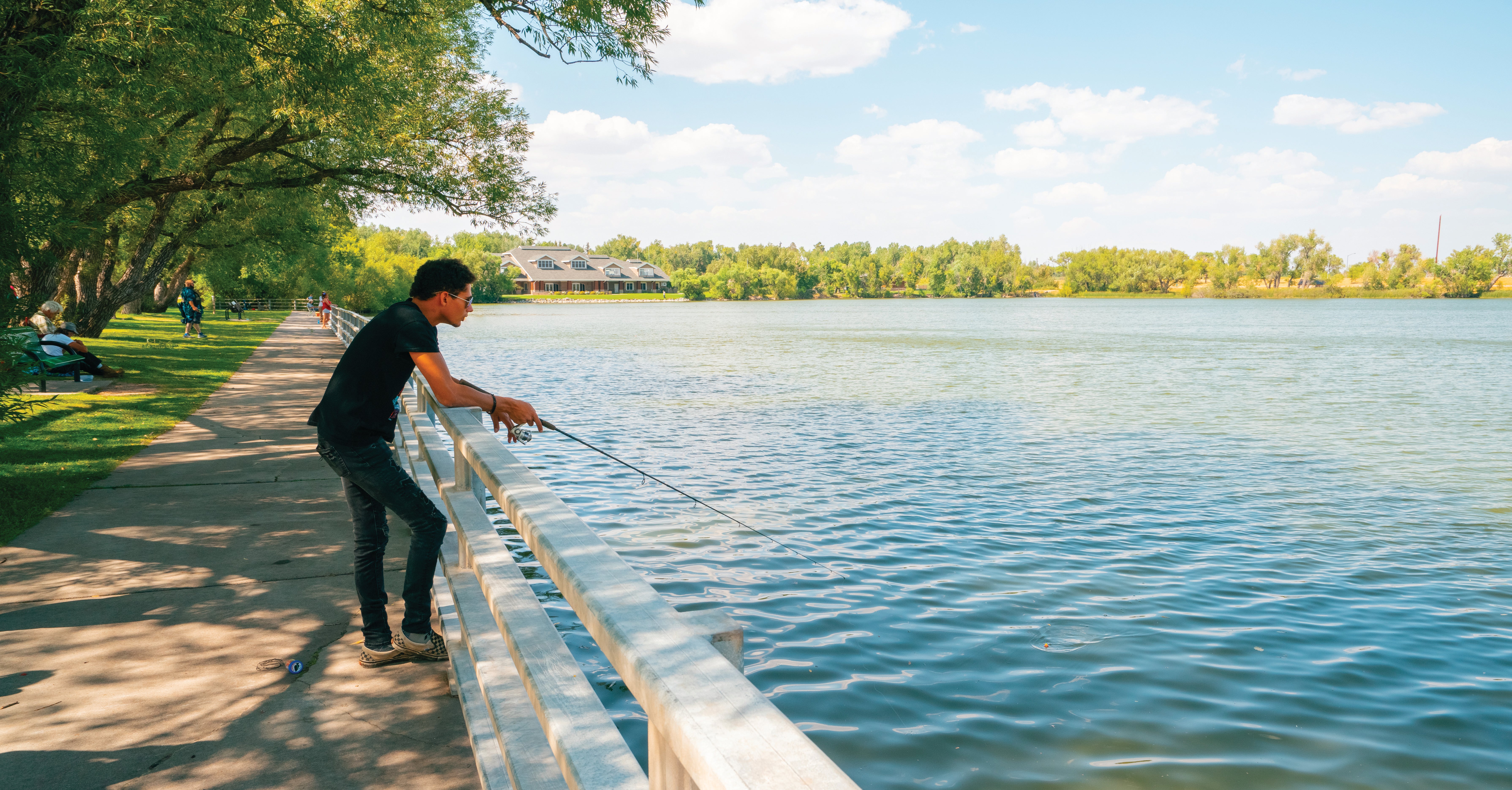 An angler rests up against a railing at the edge of Sloans lake in Cheyenne Wyoming and watches the end of his line in the water for a bite.