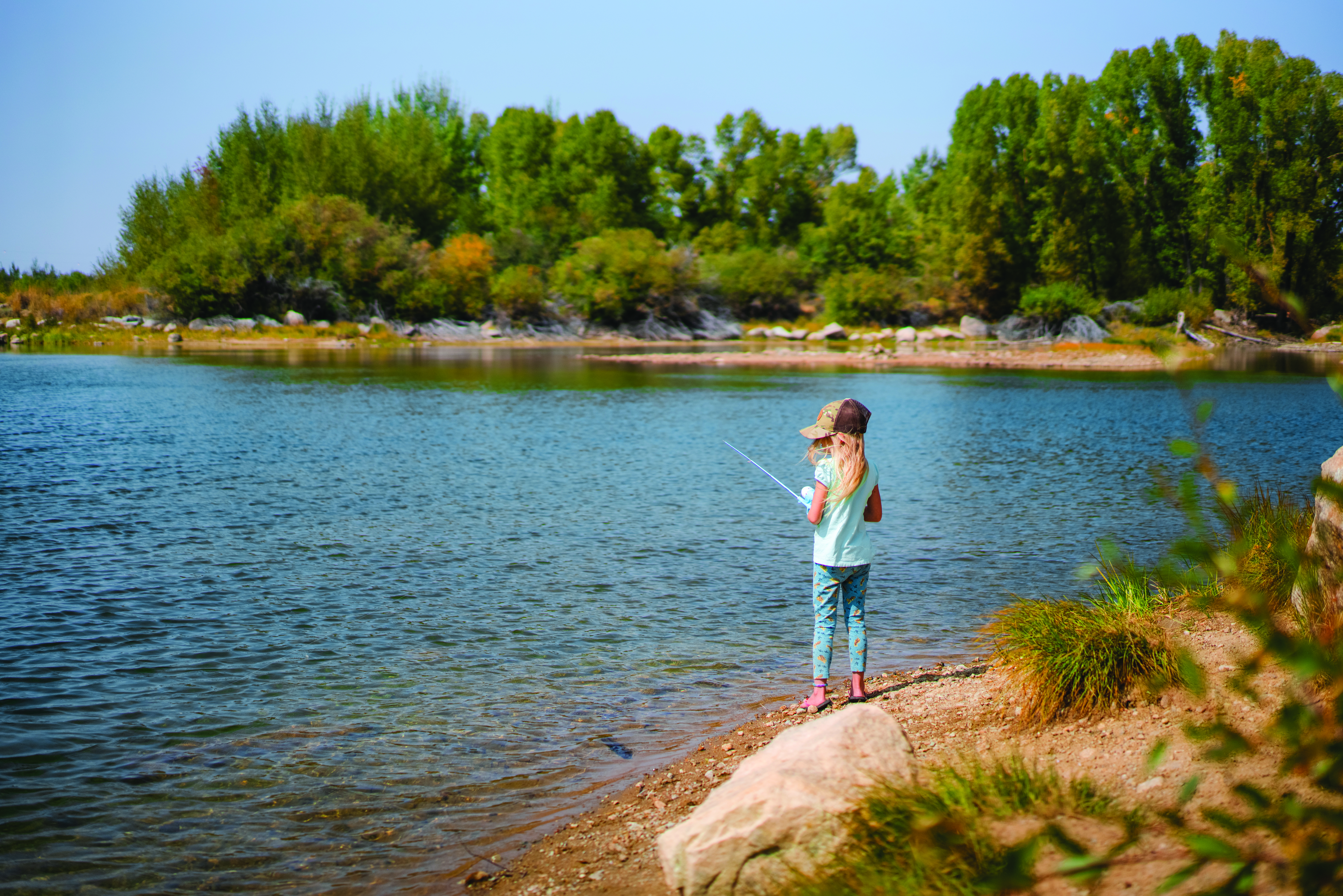 A young angler fishes the blue water of CCC Ponds near Pinedale, Wyoming from the shoreline.