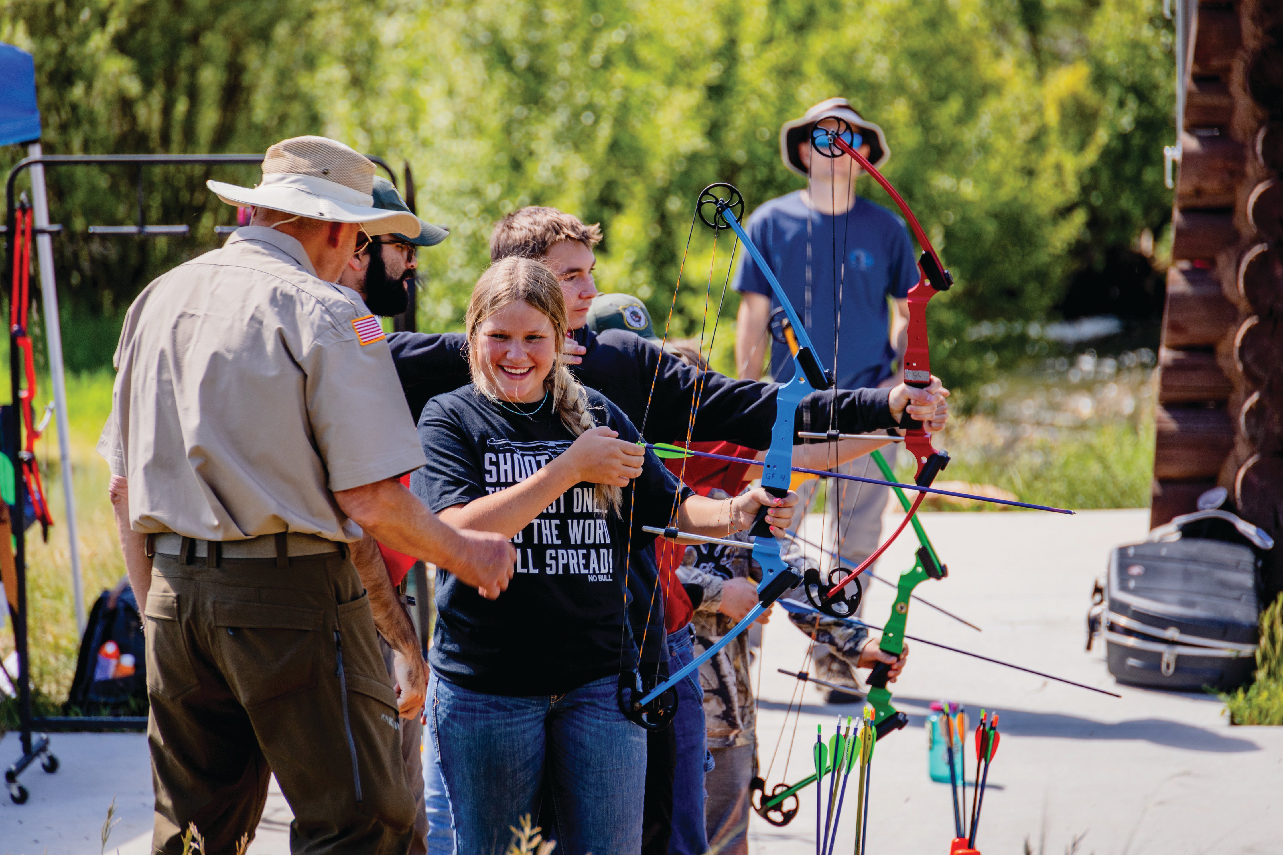 A girl gaining hands-on instruction and experience shooting a compound bow at an education event.