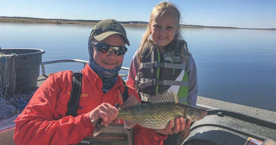 Keyhole Reservoir Fish Sampling Andrew Nikirk, fisheries biologist, holds up a walleye during a sampling on Keyhole Reservoir with his daughter, Adley.