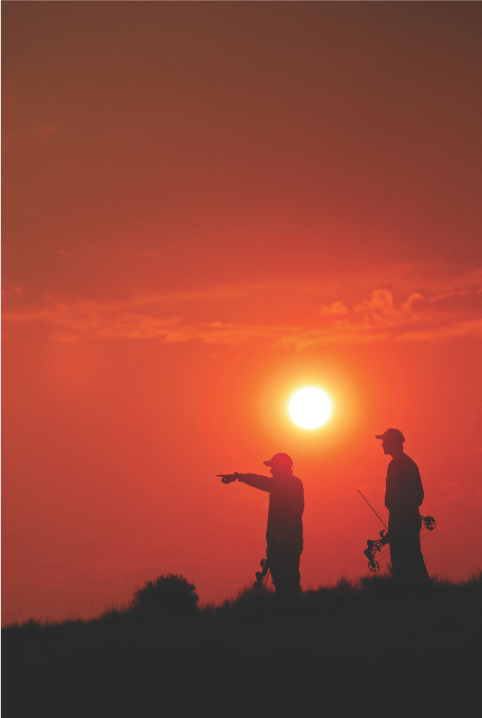 Two archery hunters hold bows, silhouetted on the horizon at sunset, with one pointing
