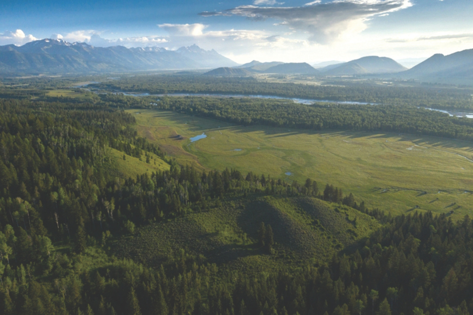 An arial photo of the Chimney Draw conservation easement, featuring trees, green meadows and distant mountain peaks
