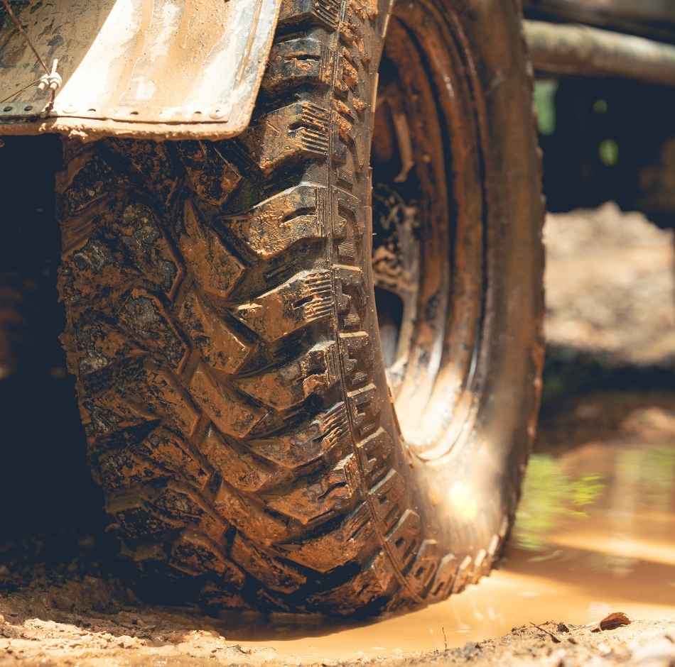 A close up of an aggressive tire of an off-road vehicle rolling through a small mud puddle.