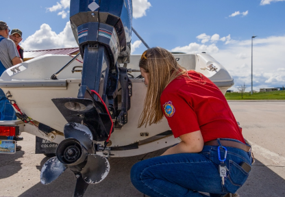 A female Game and Fish employee inspects a motorized watercraft at an aquatic invasive species watercraft check station near Cheyenne, Wyoming on a sunny day. 