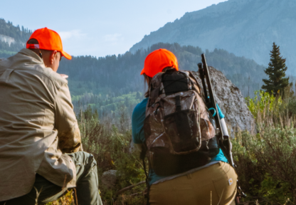 Two hunters in hunter orange hats sneak up on their quarry in a beautiful mountainous landscape.