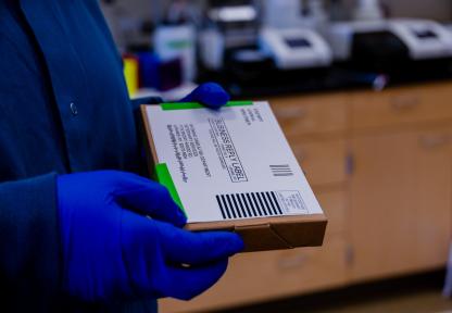 A gloved lab employee holds a mailed box containing a brucellosis sample