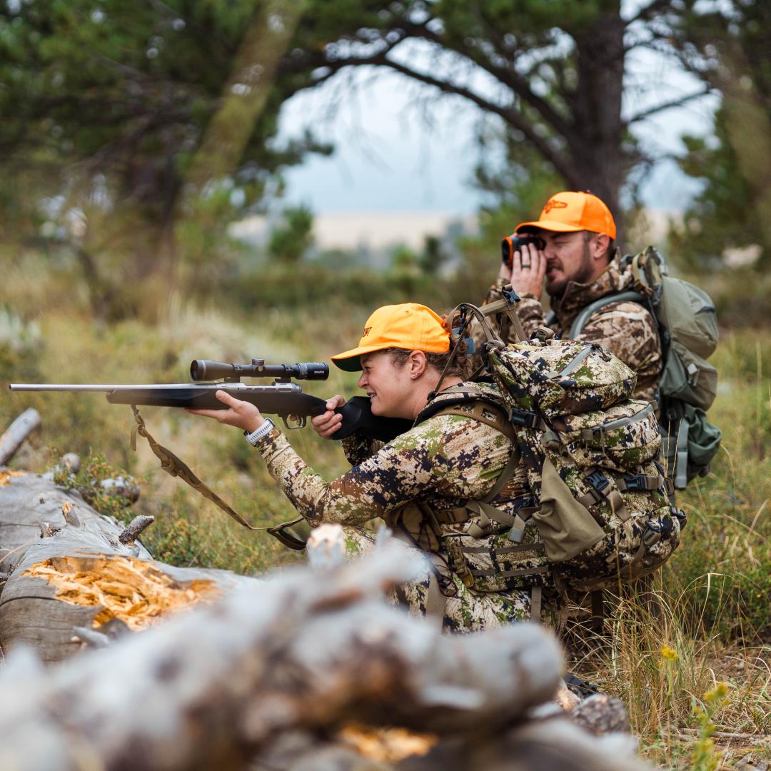 Rifle hunter looking through scope with hunting partner using range finder