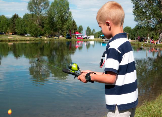 A youth angler in a blue and white horizontal striped shirt uses a spin casting rod to try to catch fish at a fishing derby