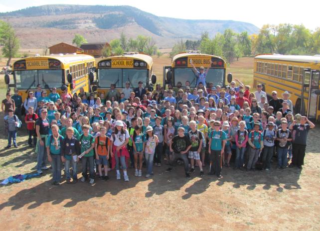 Students stand in front of yellow school busses for a group photo.