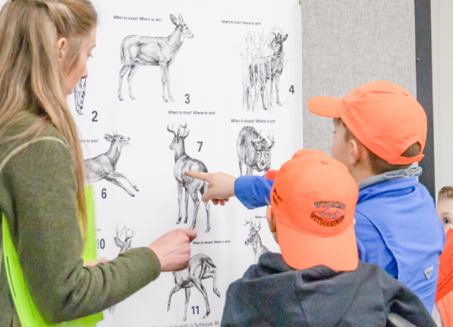 Game and Fish Hunter Education instructor teaches two students wearing hunter orange about hunting shot placement