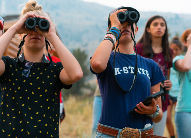 High school girls look through binoculars during a bird watching and wildlife ID session at Whiskey Mountain Conservation Camp