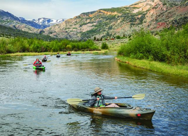 A group of women floating in kayaks down Torrey Creek with peaks of the Fitzpatrick wilderness in the background