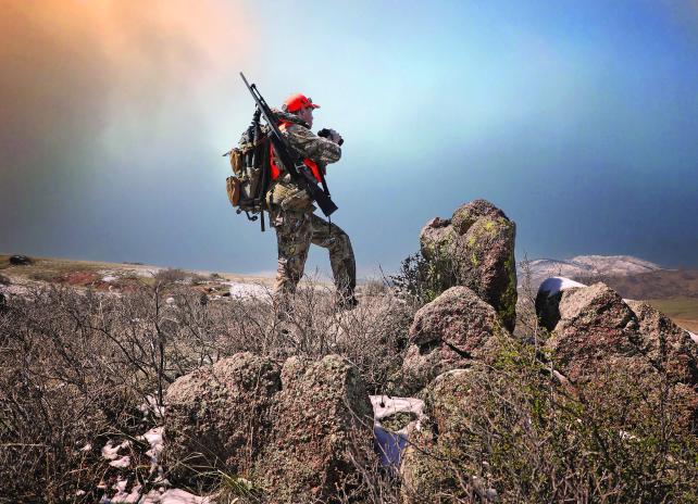 A hunter glassing an area looking for game. Hunter uses binoculars to look for game.