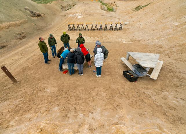 A group of students gather around a table for a safety briefing at a Wyoming shooting range.