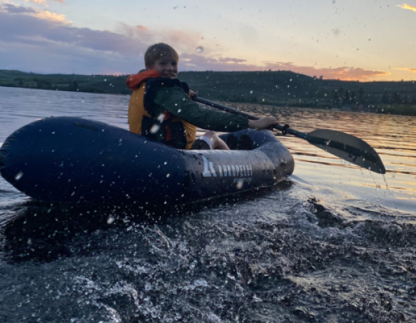 Boy paddles pack raft at sunset