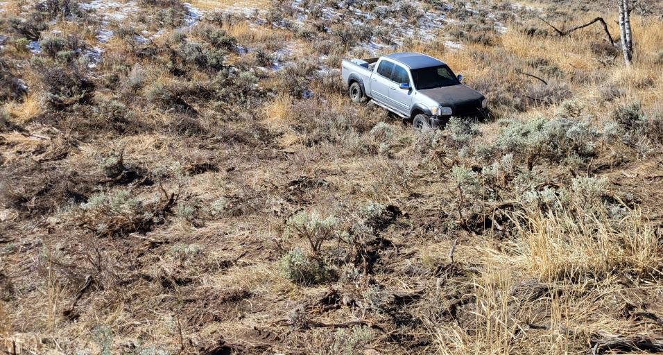 A silver pickup is stuck after driving off-road into the sagebrush.