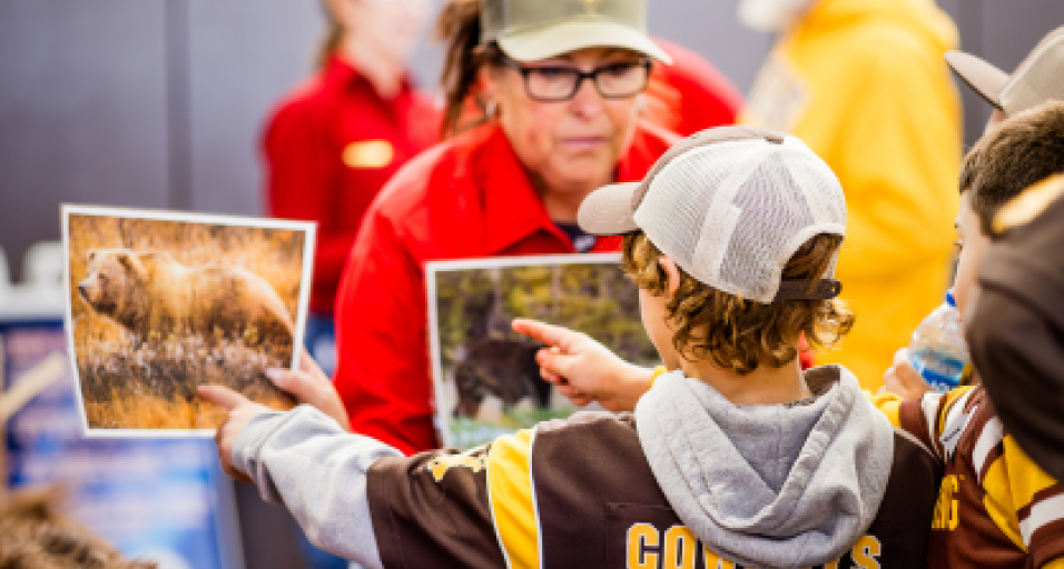 A Wyoming Game and Fish Department Employee ask a kid in a University of Wyoming Cowboys jersey to identify the type of bears shown on two different pieces of paper