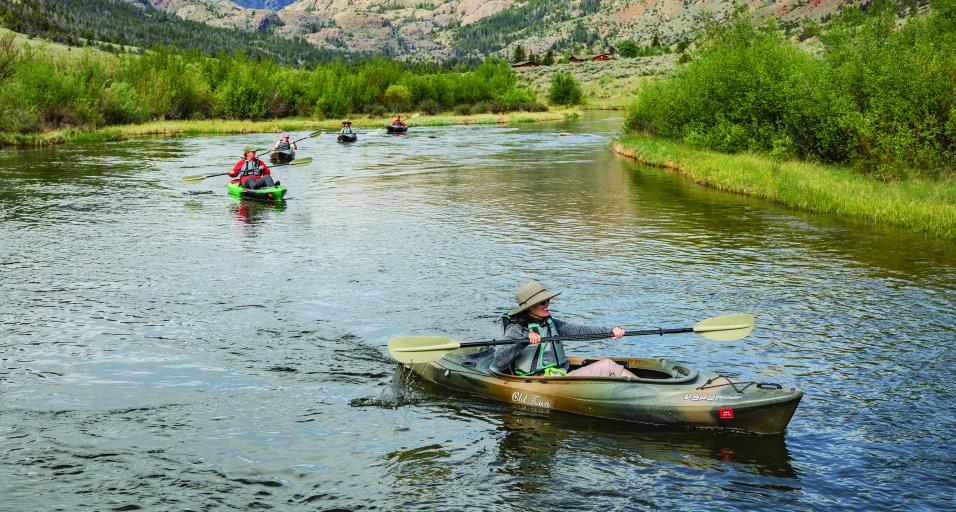 A group of women floating in kayaks down Torrey Creek with peaks of the Fitzpatrick wilderness in the background