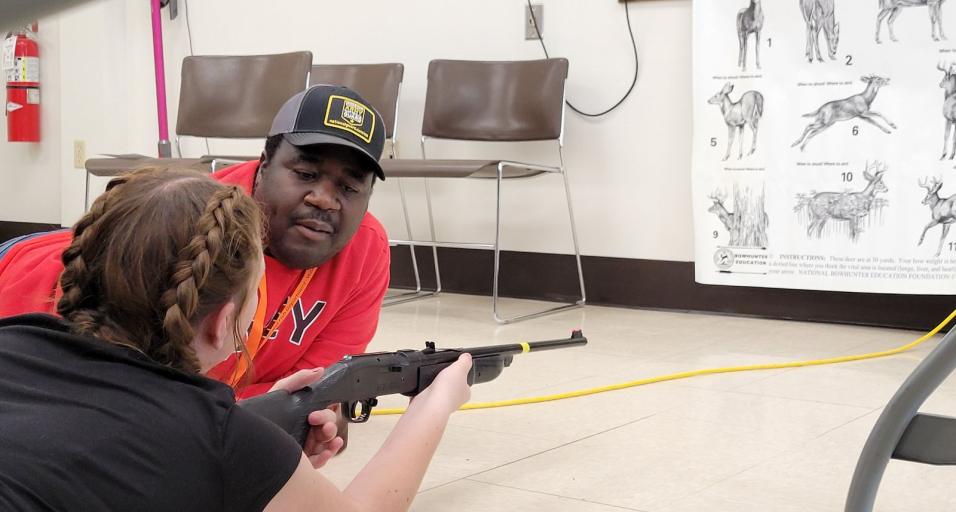 Hunter education instructor helps a student with shooting position