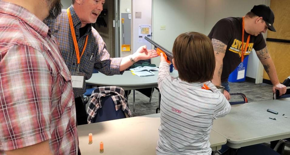 Student learning weapon safety during hunter's ed course with two instructors