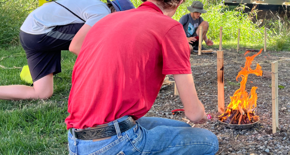 An outdoor day participant practices fire building skills at an outdoor survival learning station  