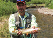 Male angler wearing a hat and fishing vest holds a bonneville cutthroat trout for a photo