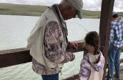 A volunteer assists a participant at the 2024 Kids Fishing Day with baiting a hook. 