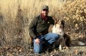 Ty Masco, Wyoming Game and Fish Department game warden kneeling next to his dog. 