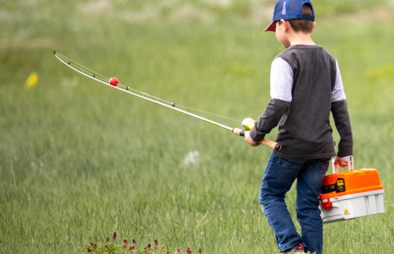 A kid with a fishing pole and tacklebox walks through a field