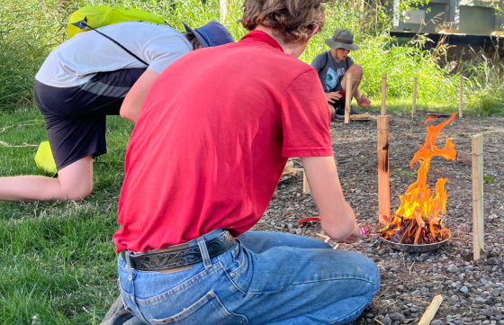 An outdoor day participant practices fire building skills at an outdoor survival learning station  