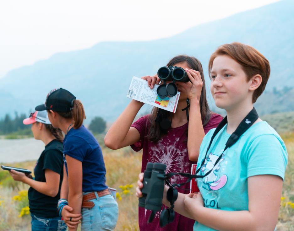 A girl looks a wildlife through binoculars at a Game and Fish youth camp at the Whiskey Mountain Conservation Camp