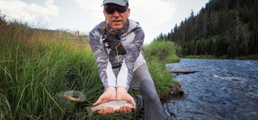 Male angler holding a Snake River Cutthroat trout with a river in the background as part of Wyoming's Cutt Slam Fishing Challenge