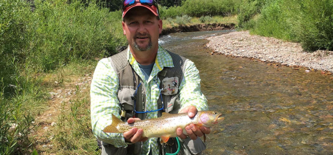 Male angler wearing a hat and fishing vest holds a bonneville cutthroat trout for a photo