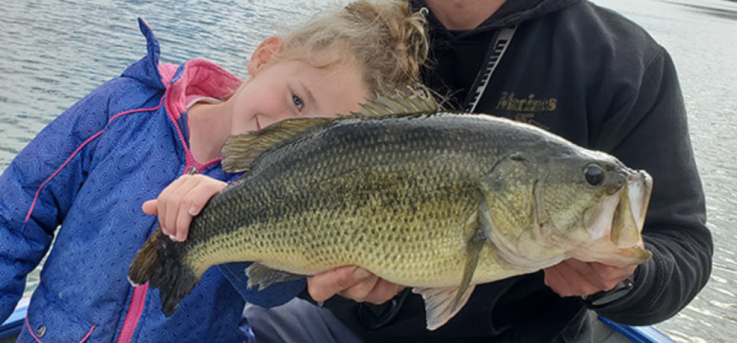 Youth angler leans behind a Master Angler sized largemouth bass held by her father
