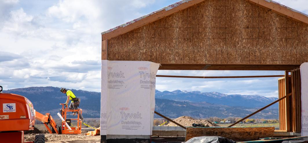 A construction worker on a lift next to an unfinished structure that the viewer can look through to see mountains off in the background.