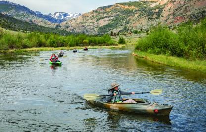 A group of women floating in kayaks down Torrey Creek with peaks of the Fitzpatrick wilderness in the background