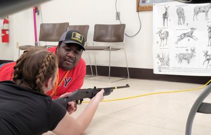 Hunter education instructor helps a student with shooting position