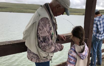 A volunteer assists a participant at the 2024 Kids Fishing Day with baiting a hook. 