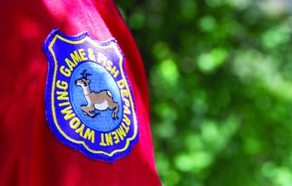 A photo of the patch on the shoulder of a Game and Fish Employee's uniform in front of green foliage in the background.