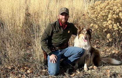 Ty Masco, Wyoming Game and Fish Department game warden kneeling next to his dog. 