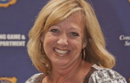 A woman smiles in front of a navy blue background 