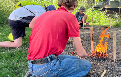 An outdoor day participant practices fire building skills at an outdoor survival learning station  