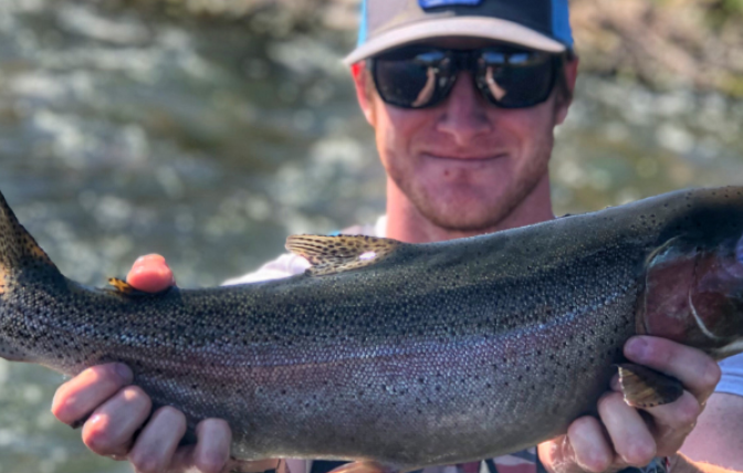 Male angler holds a large rainbow trout for a photo